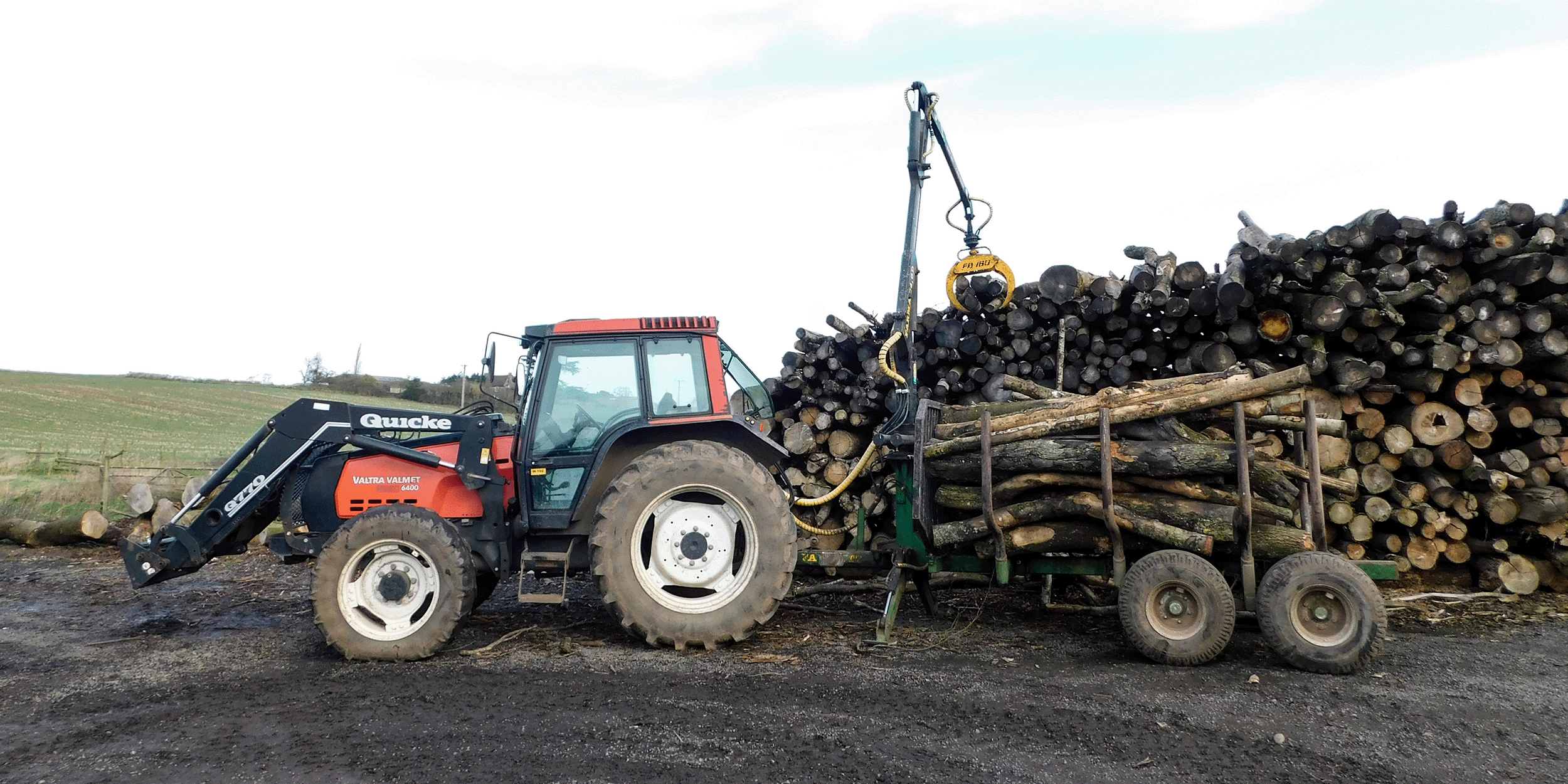 A tractor at a wood fuel production site with stacked cut trees